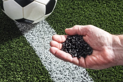 Hand holding crumb rubber over a turf soccer field.
